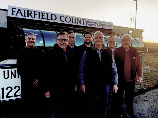 group of men standing together in front of airport signage